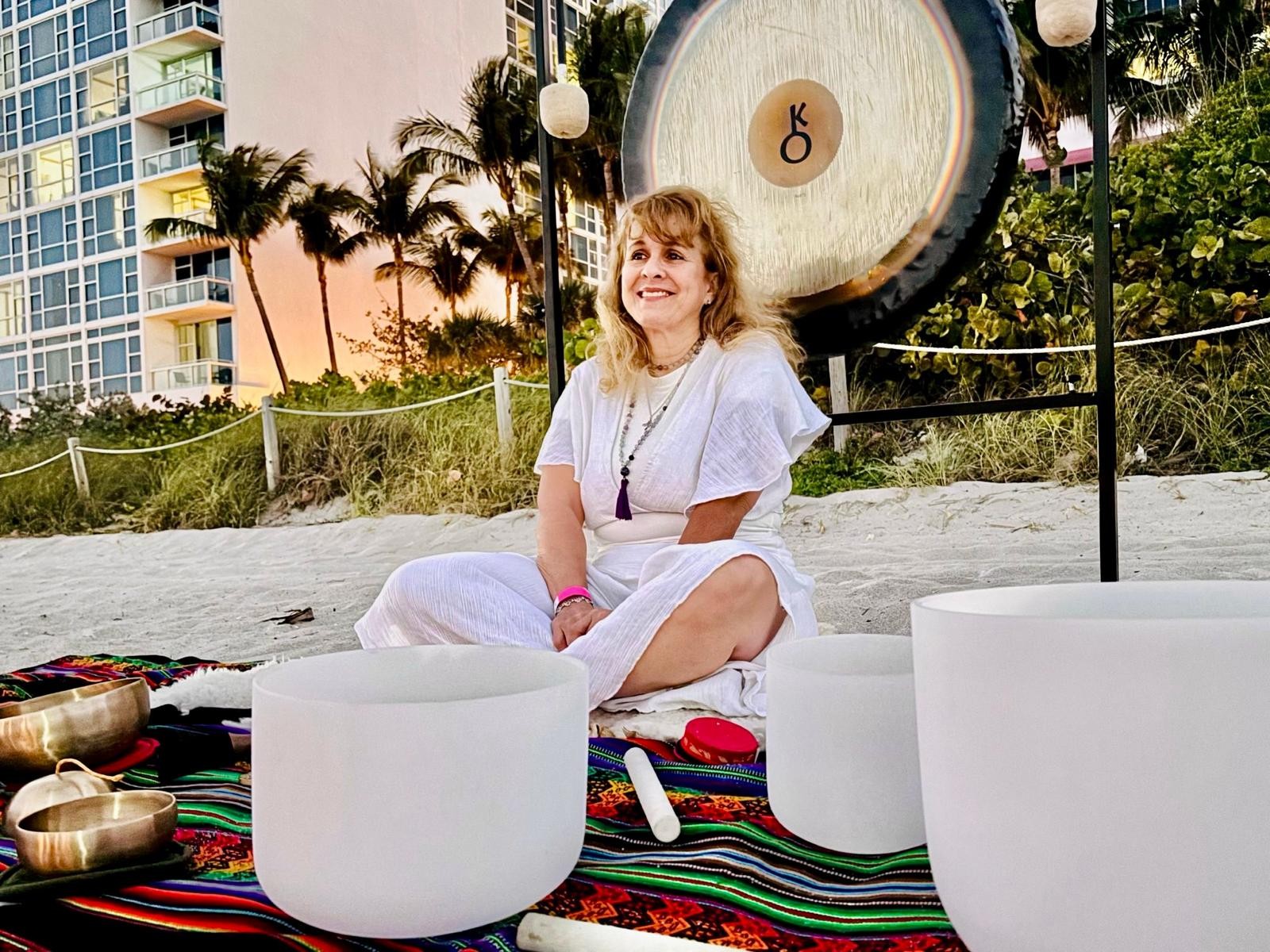 Diana smiling on a South Florida beach in front of the Chiron gong with quartz crystal and Tibetan singing bowls