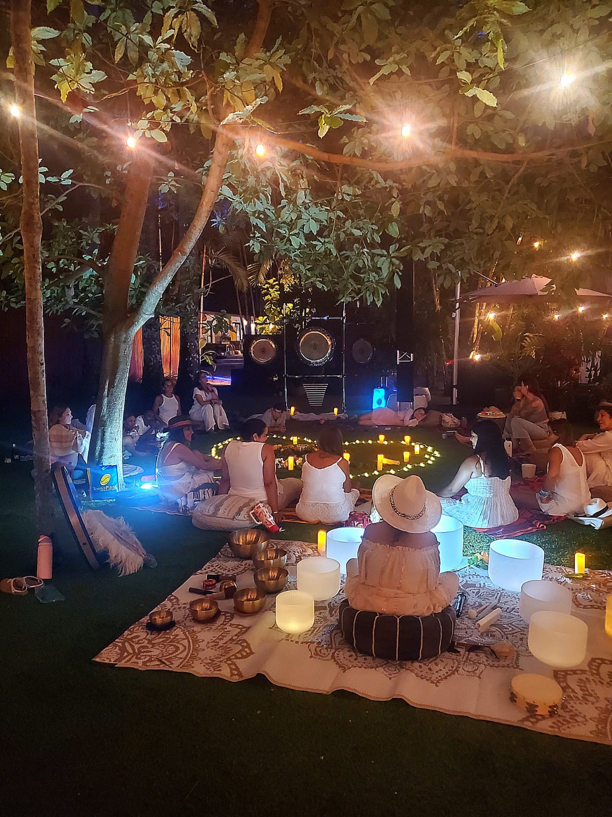 A community gathered beneath illuminated garden trees for a candlelit sound bath with crystal and Tibetan bowls