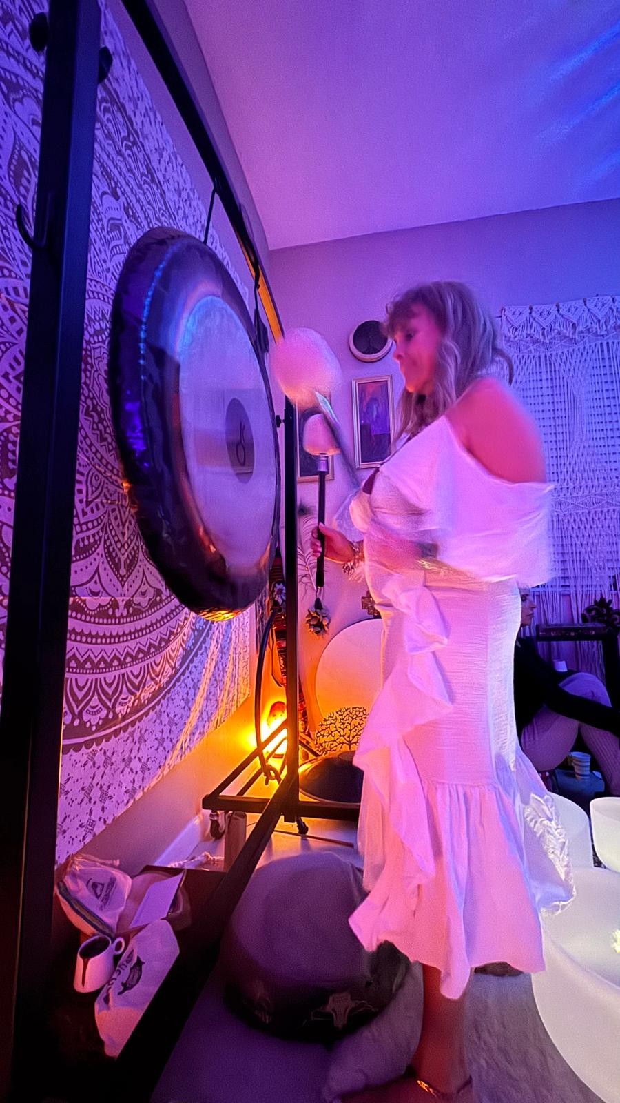 Diana playing a gong beside singing bowls in vibrant violet and indigo ambient light