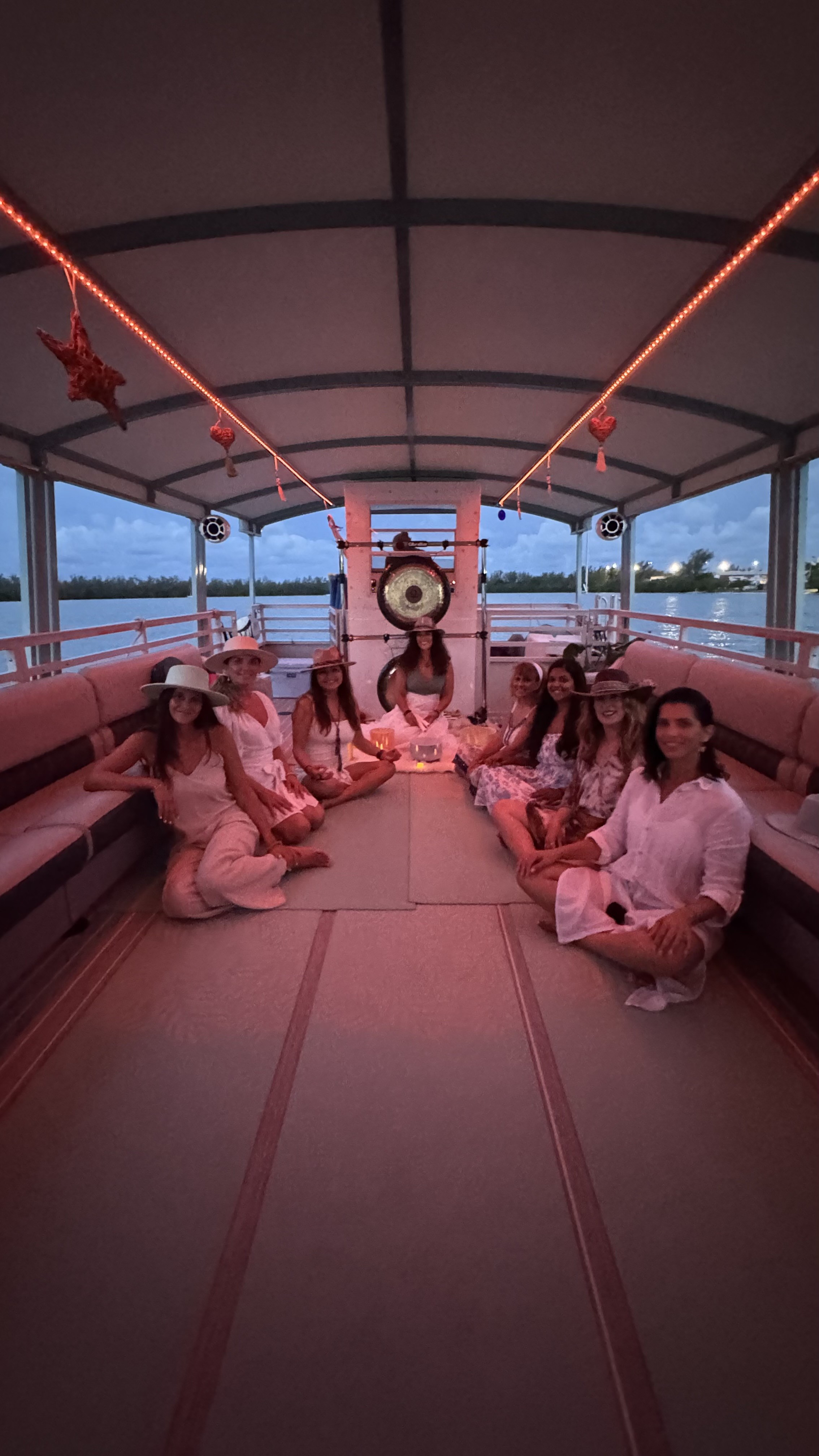 A group dressed in white gathered aboard a boat at sunset around Diana and a bow gong