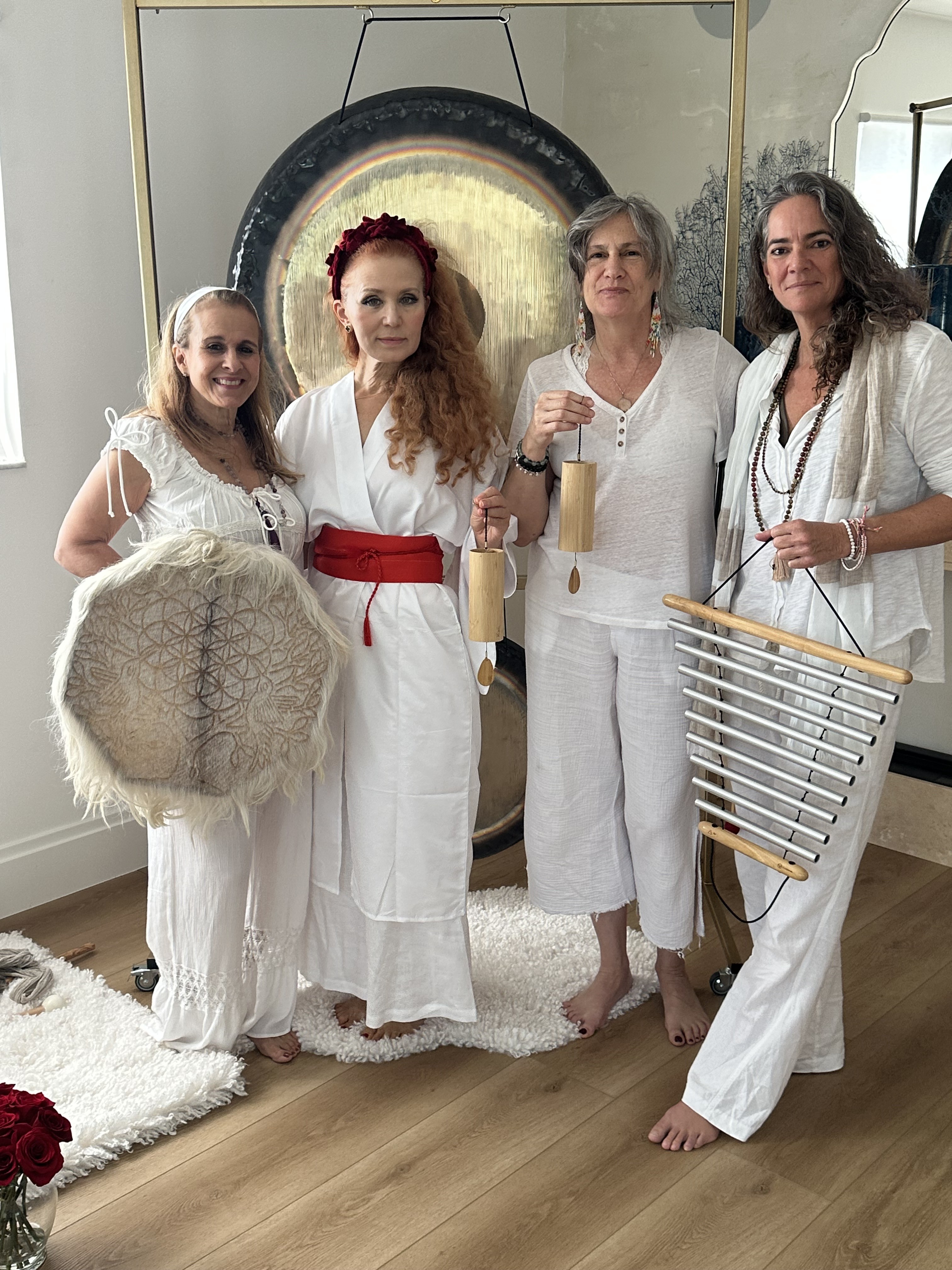 Four sound practitioners dressed in white holding a sacred drum, Koshi chimes, and bar chimes in front of a gong at the Gong 4 All event