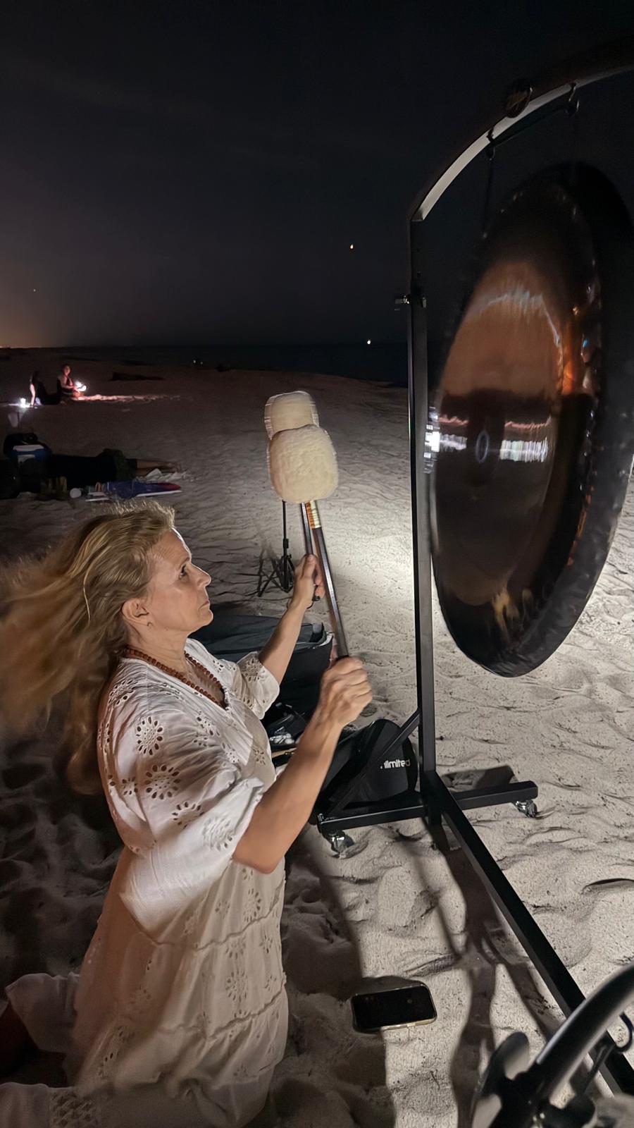 Diana playing a planetary gong on the beach beneath the night sky